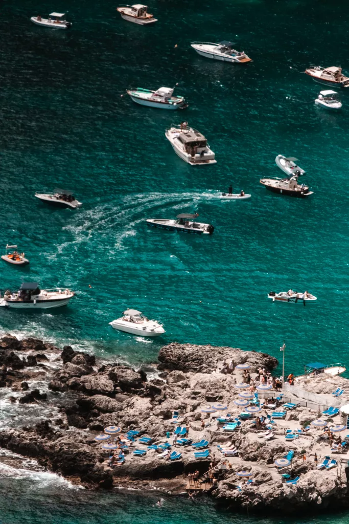 View of the water of Capri Italy on day trip from Sorrento. Boats in water and sun lounges on rocks